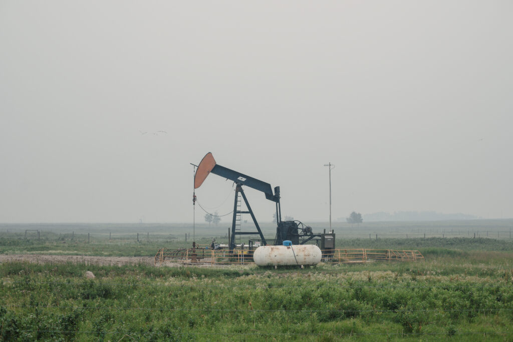 A pumpjack sits in a smoky field in Alberta