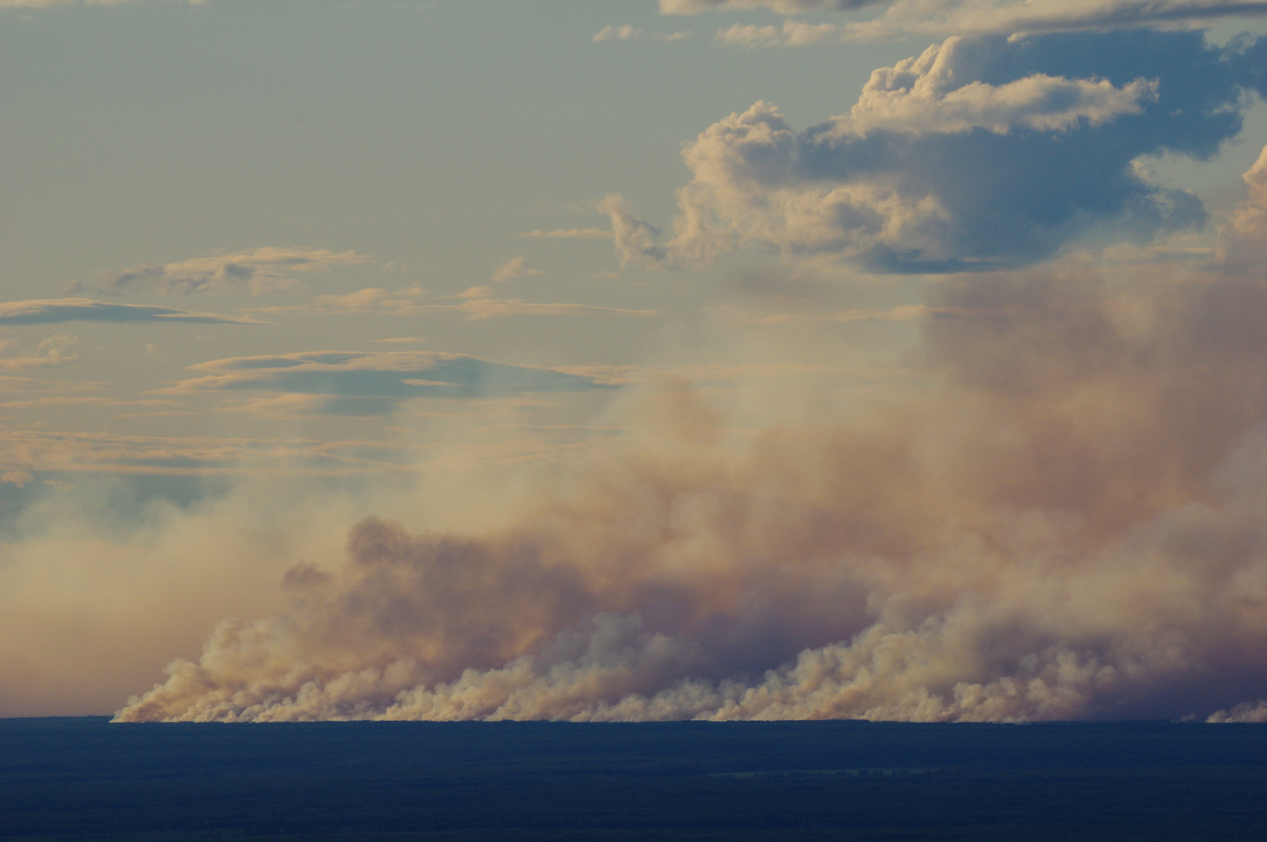 Smoke from a line of 2019 Alberta wildfires stretches above a flat horizon