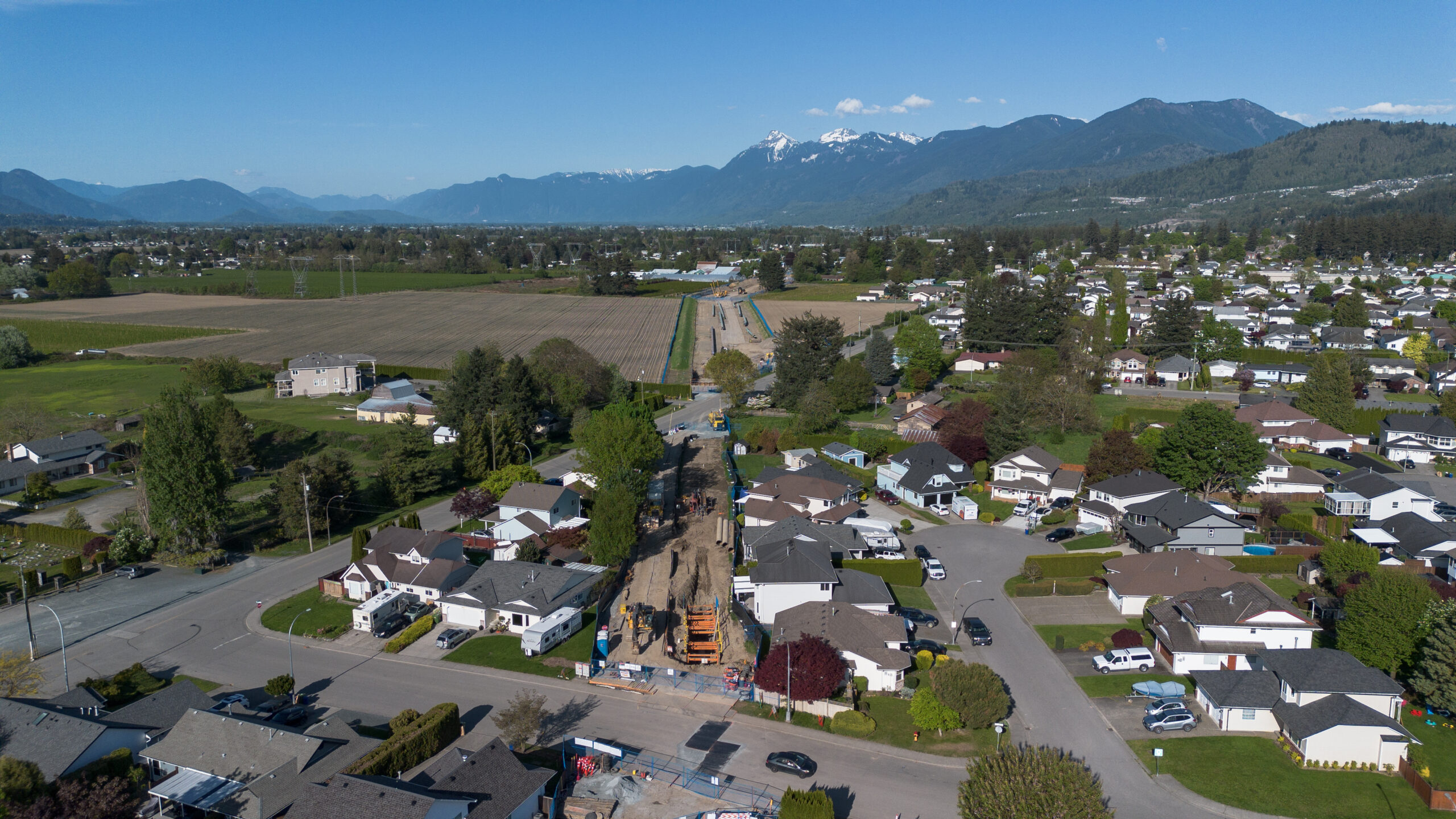Aerial view of a suburb and construction of a pipeline cutting through a neighbourhood with mountains in the background.