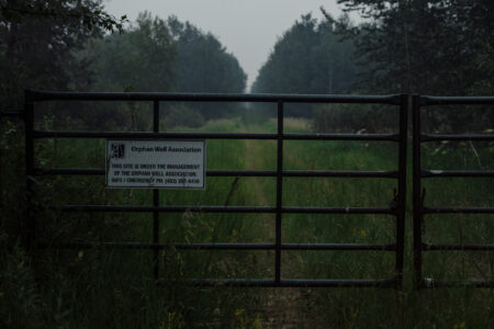 A sign for Alberta's Orphan Well Association on a gate leading to a well site with where the company has walked away