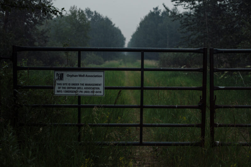 A sign for Alberta's Orphan Well Association on a gate leading to a well site with where the company has walked away