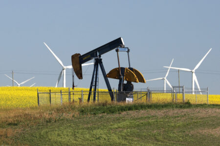 An oil pumpjack in a field, with wind turbines in the background