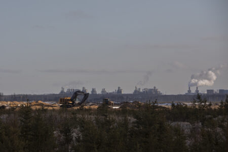 An excavator on a hill, with the Fort Hills oilsands mine in the background