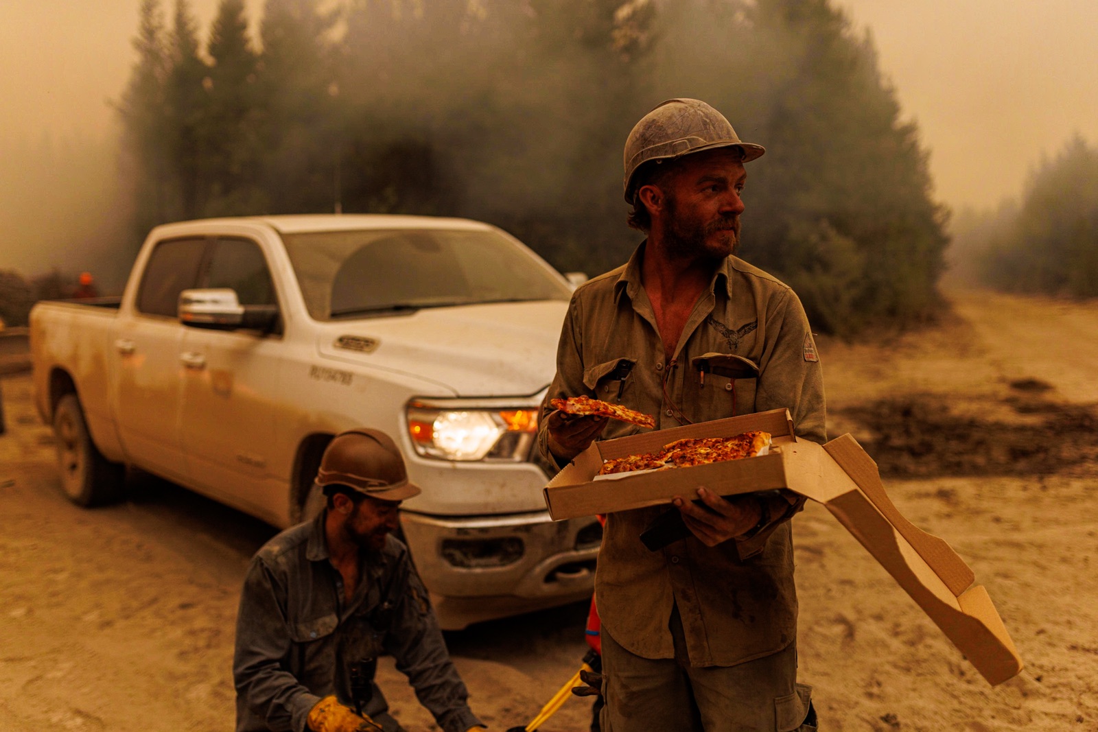 BC Wildfire: a firefighter with the Alaska Smoke Jumpers eats a pizza near a pickup truck in a smoky forest