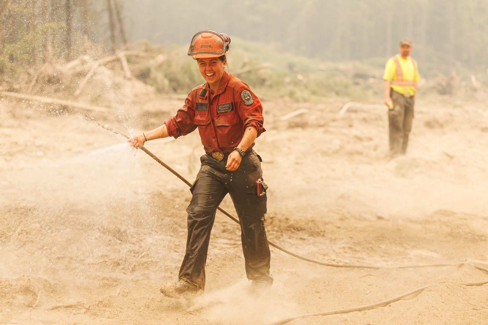 BC Wildfire: A firefighter laughs as she tries to wrangle an unruly fire hose that's leaking