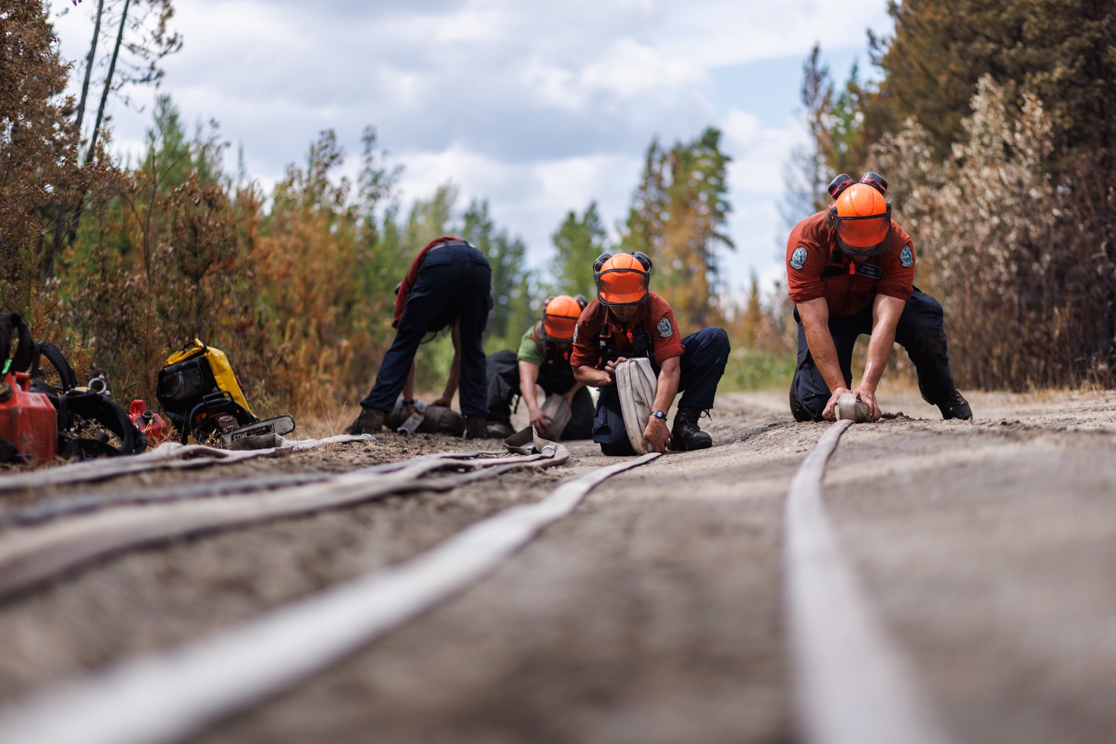 BC wildfire: firefighters role hoses, with trees in the background