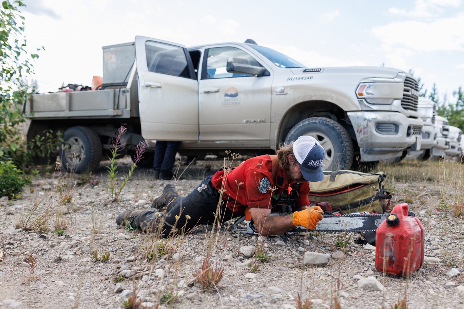 A sawyer sharpens his chainsaw next to a row of trucks 