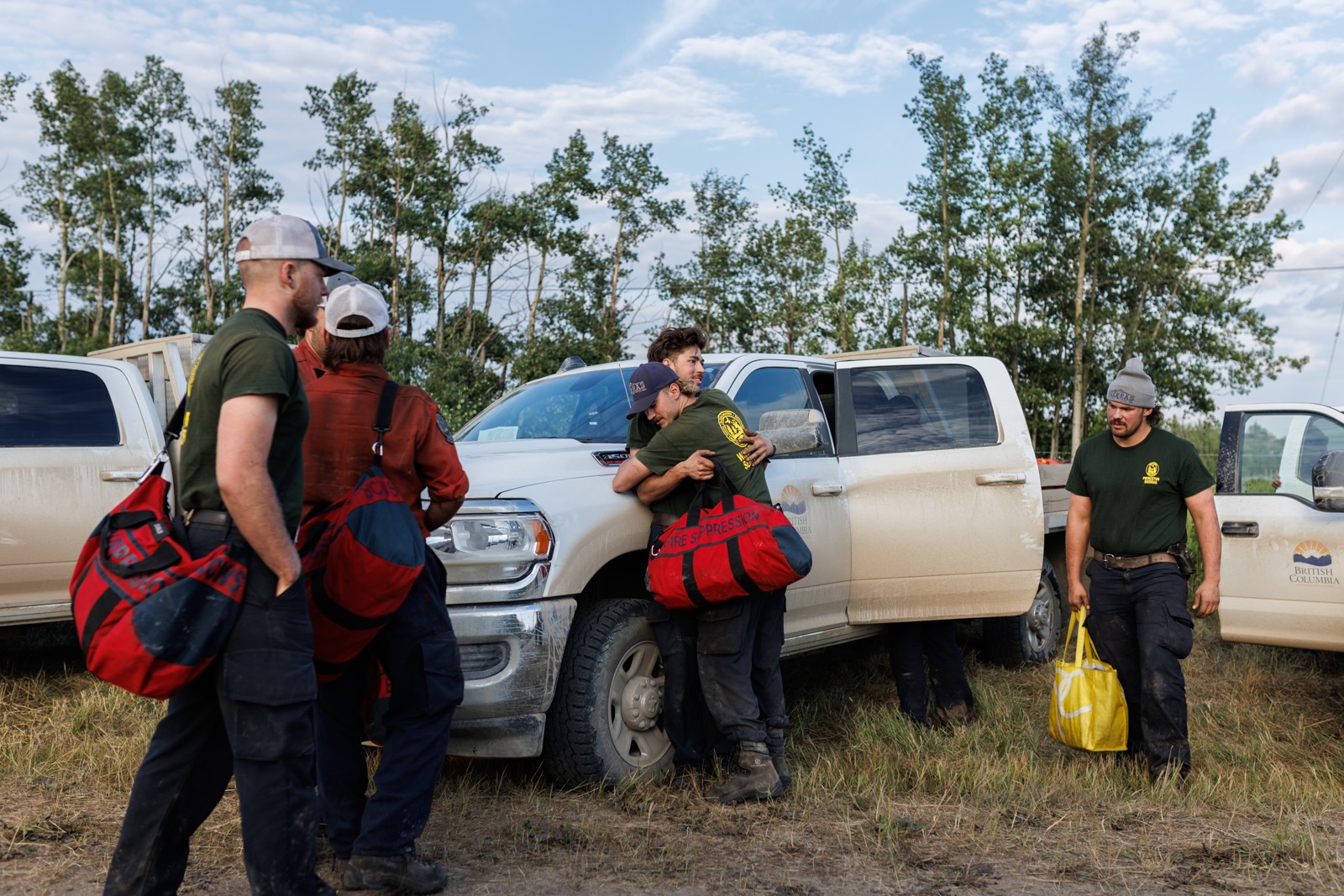 BC wildfire: Two firefighters hug as others, with bags slung over the shoulders stand nearby a group of trucks