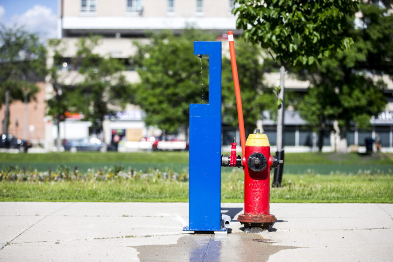 A blue water station connected to a red fire hydrant drips water in downtown Winnipeg