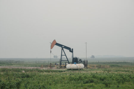 A pumpjack sits in an Alberta field with hazy skies.