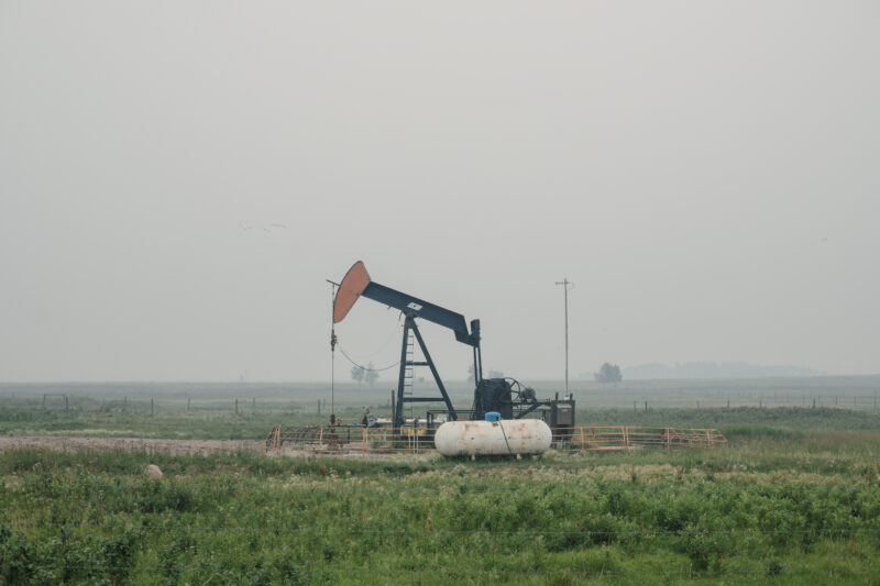A pumpjack sits in an Alberta field with hazy skies.