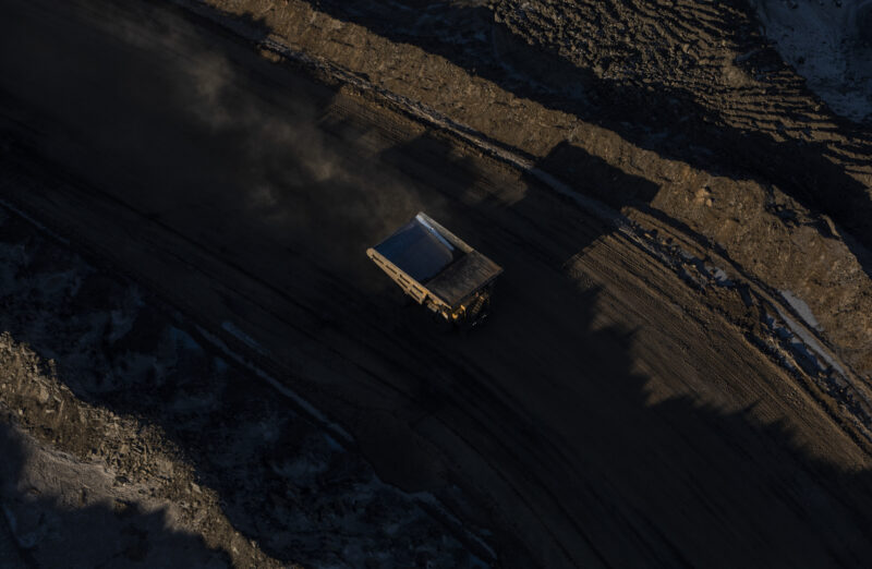 An oilsands mining truck seen from above drives down a dark dirt road.