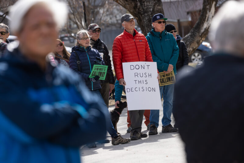 A man standing with a sign that reads "DON'T RUSH THIS DECISION." People around him have smaller signs that read "Say No Way to Galloway"