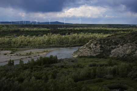Wind turbines on the horizon with mountains in the background and a river valley in the foreground.
