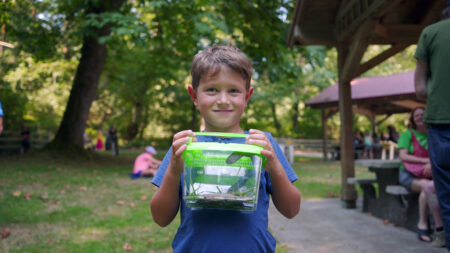 A boy holds up a box with his slug and smiles for the camera.