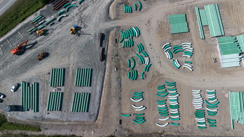 Aerial shot of green pipeline segments lying in the dirt and gravel.