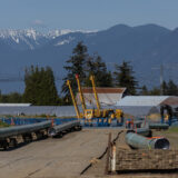 Pipeline construction near a highway with mountains in the background.