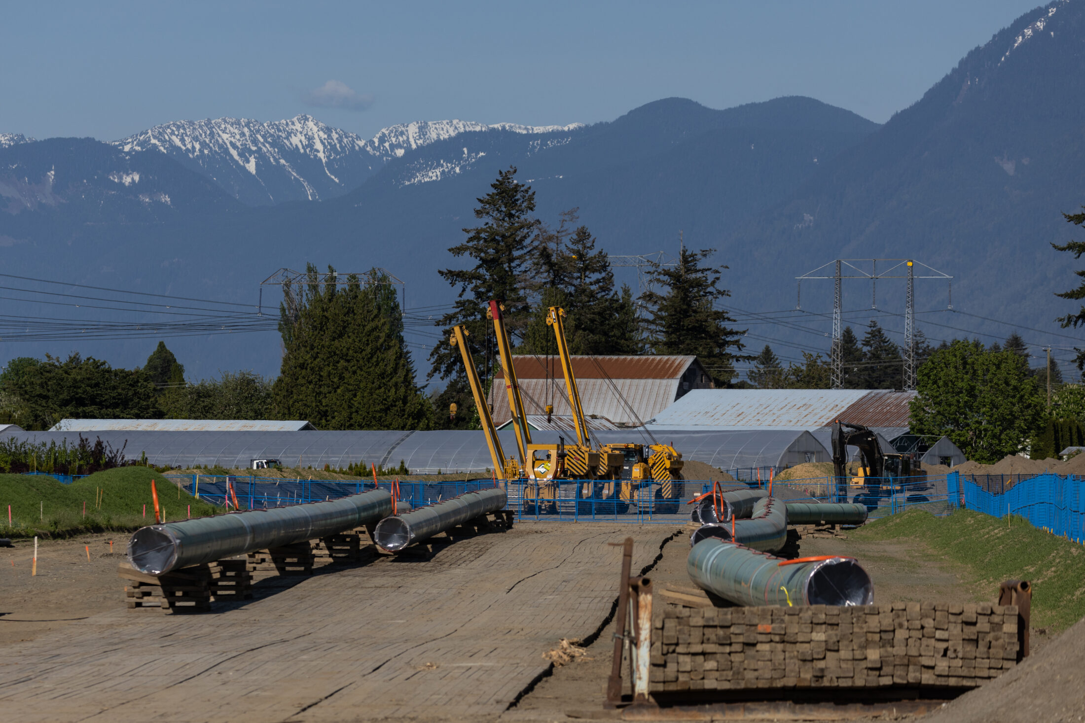 Pipeline construction near a highway with mountains in the background.