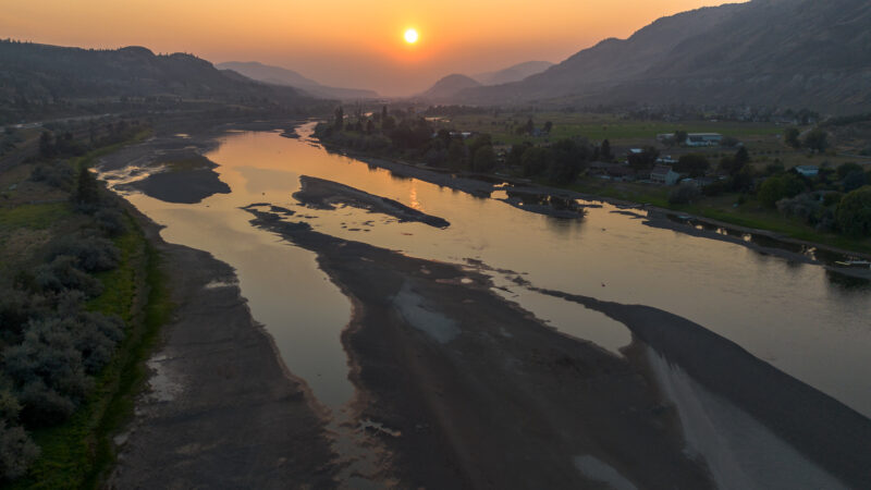 Under an orange, smoky sunset just outside of Kamloops B.C., the Thompson River is low, slow and glassy - completely still and smooth while experiencing historically low water levels.