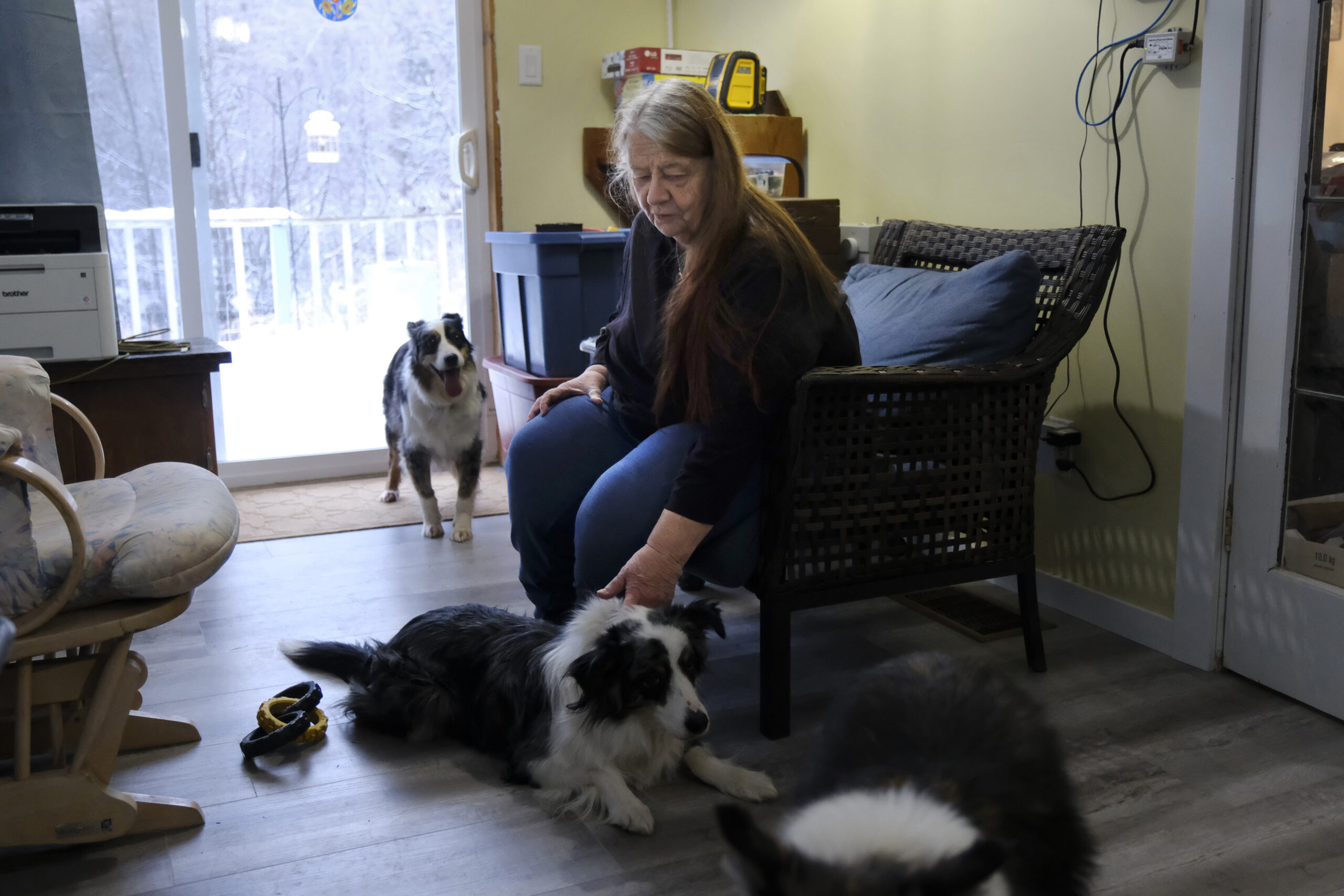 Dian Brooks sits in a wicker chair with her two dogs nearby