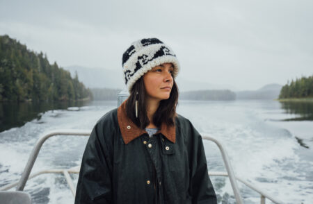 Jess Housty stands on a boat touring Heiltsuk territory, with a misty sky in the background and pale grey water marked with white foam
