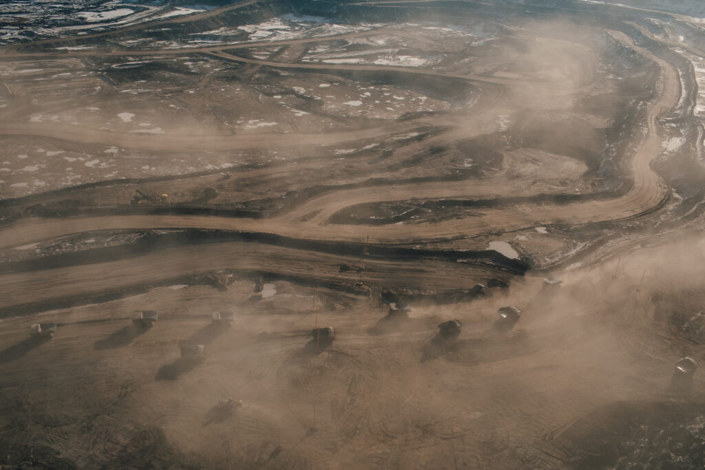 Many dumptrucks , obscured by dust and plumes, on a road at Suncor Fort Hills in Alberta oilsands