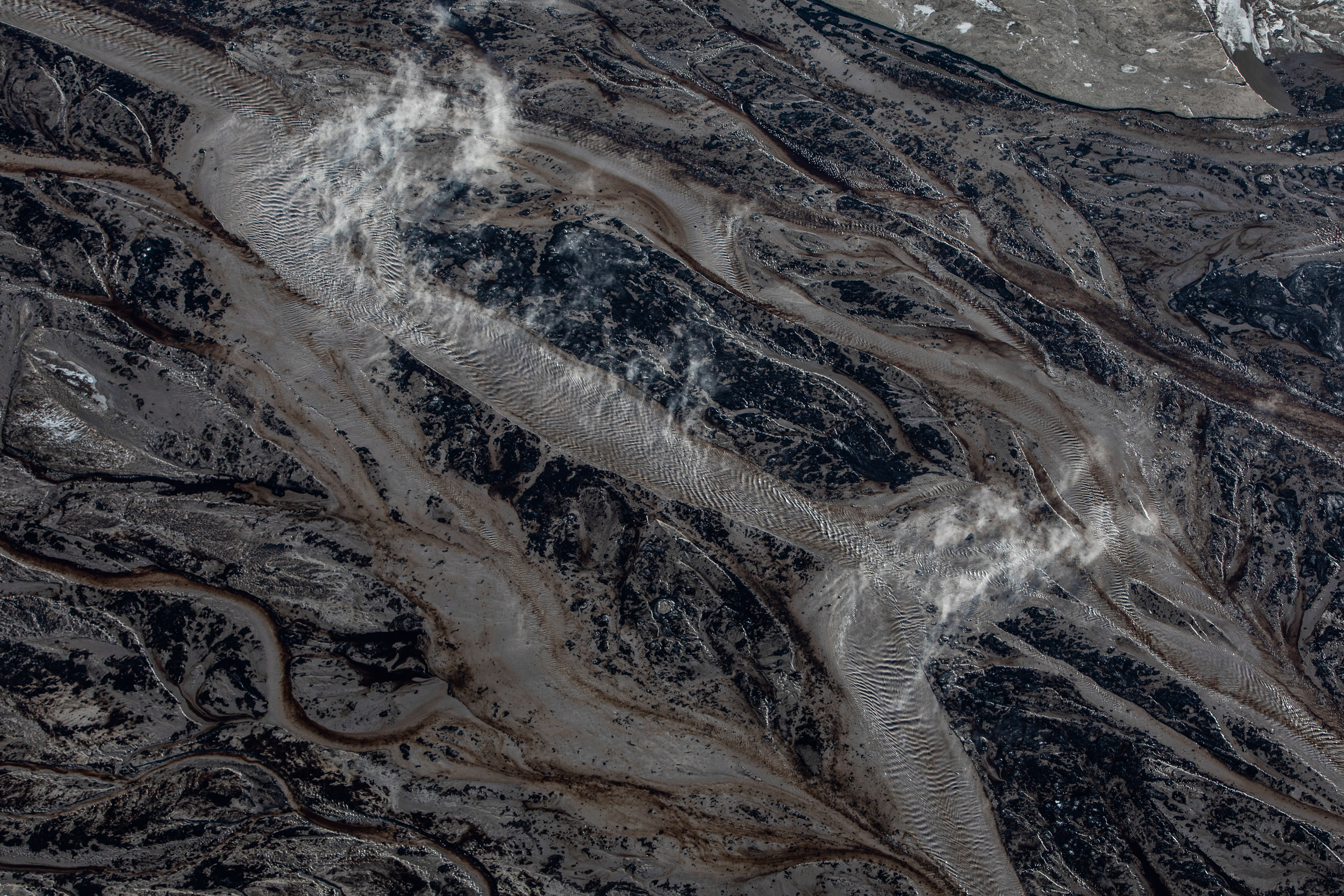Steam rises above brown liquid in a tailings pond at a Suncor open pit oilsands mine in the middle of winter