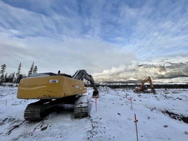 Excavators parked on snow-covered soil surrounded by mountains and conifers, where work is already on The Gateway, an already approved commercial development owned by Three Sisters Mountain Village