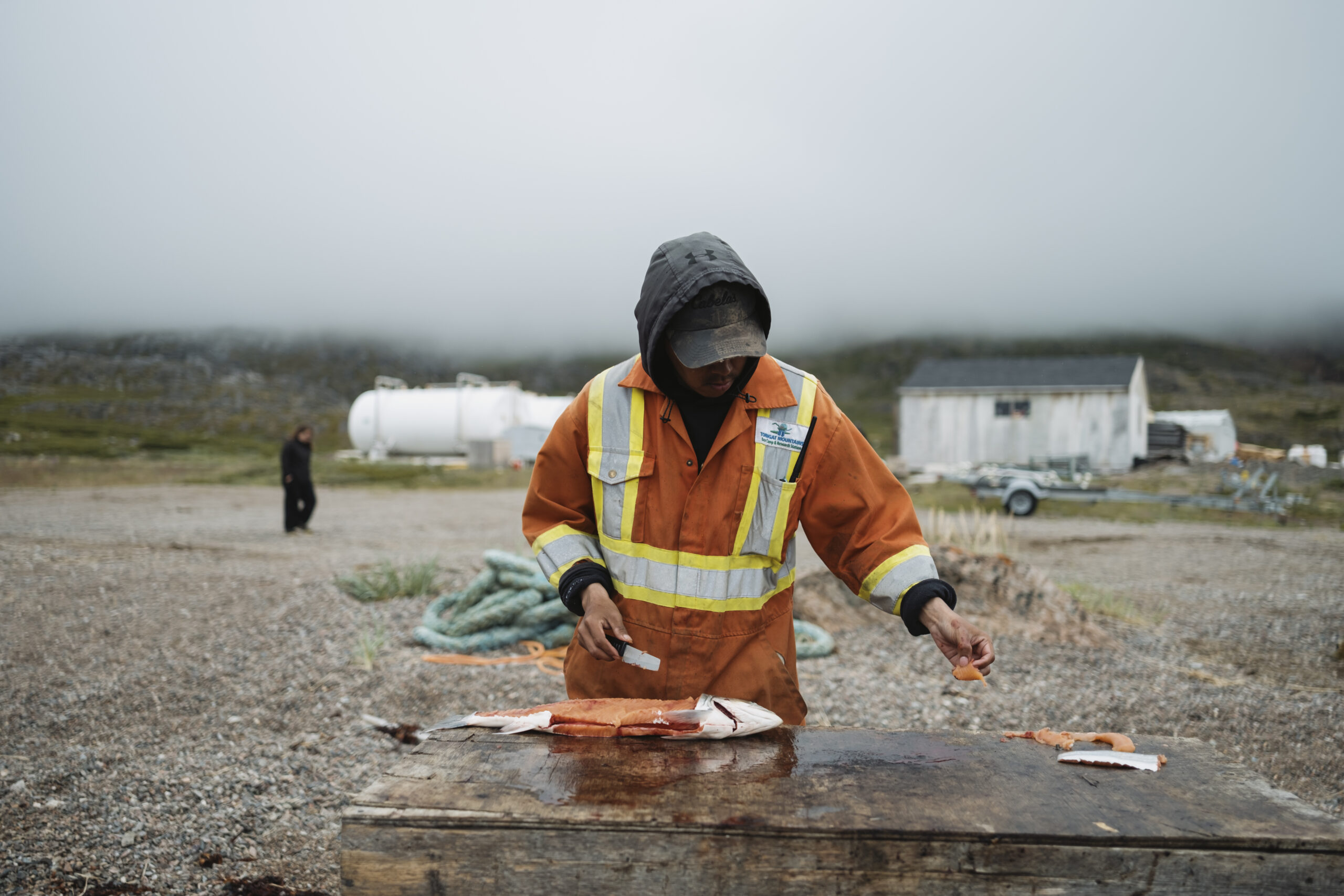 A man in a high-visibility suit fillets an Arctic char on a table outdoors