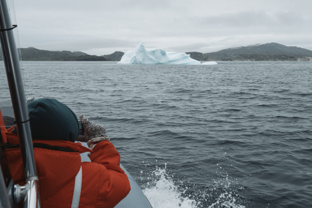Person in lifejacket takes a photo of an iceberg in the distance