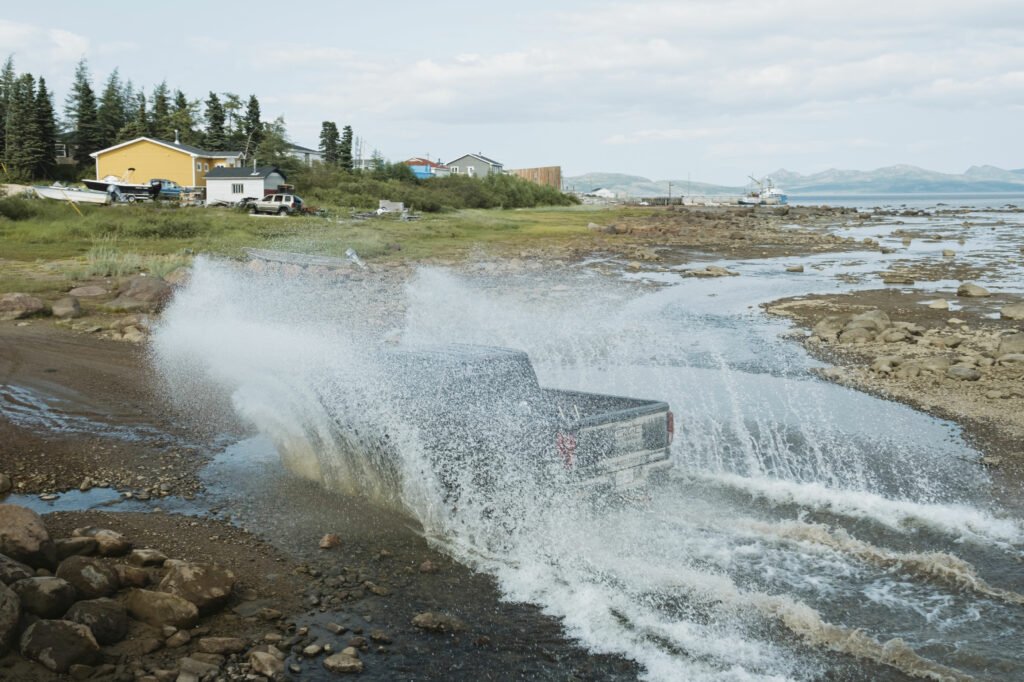 A pickup truck drives through a creek as the tide retreats from the harbour in Nain, Labrador