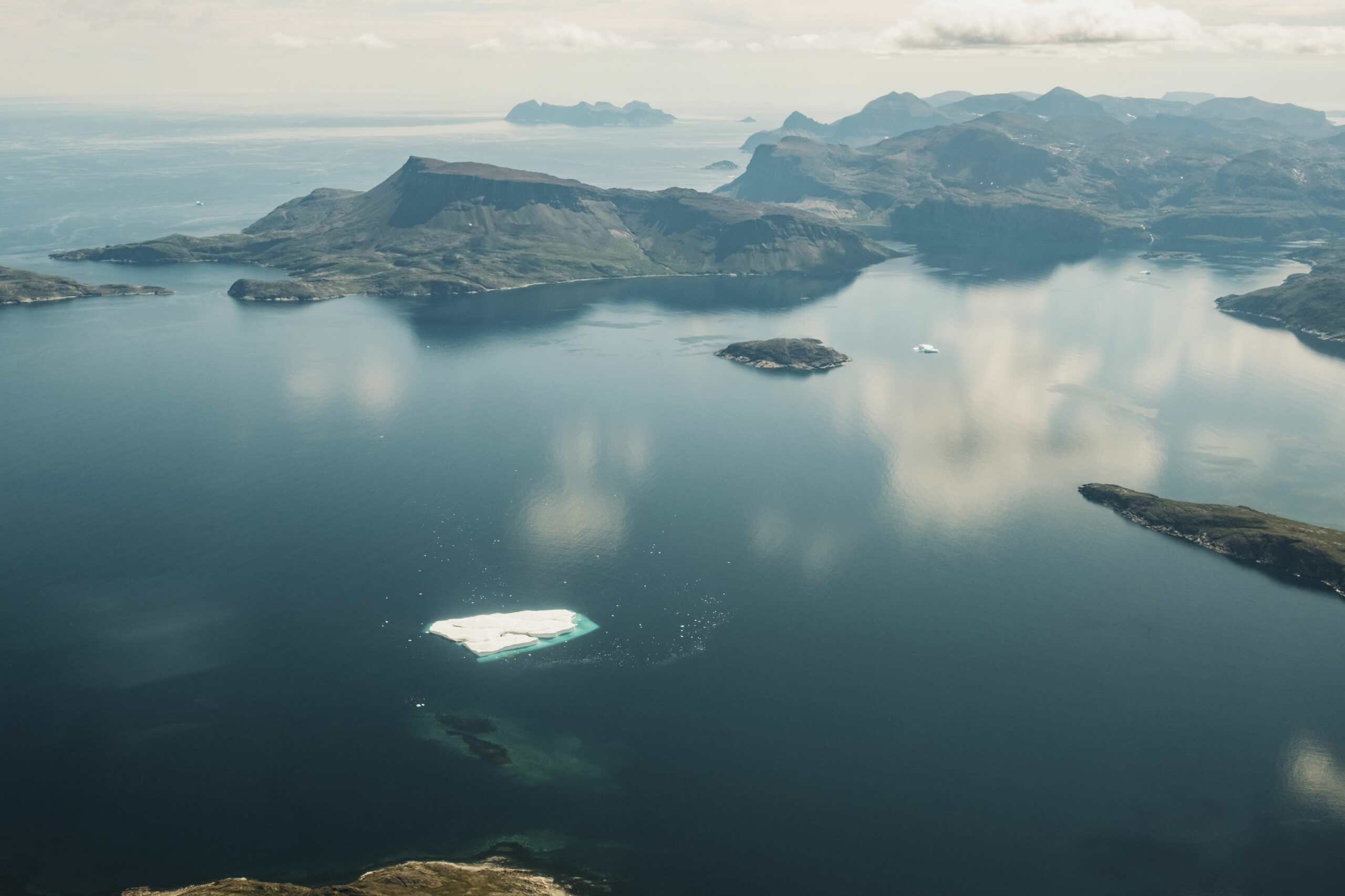 Iceberg broken up off the shore with rocky hills around it on the Labrador Sea