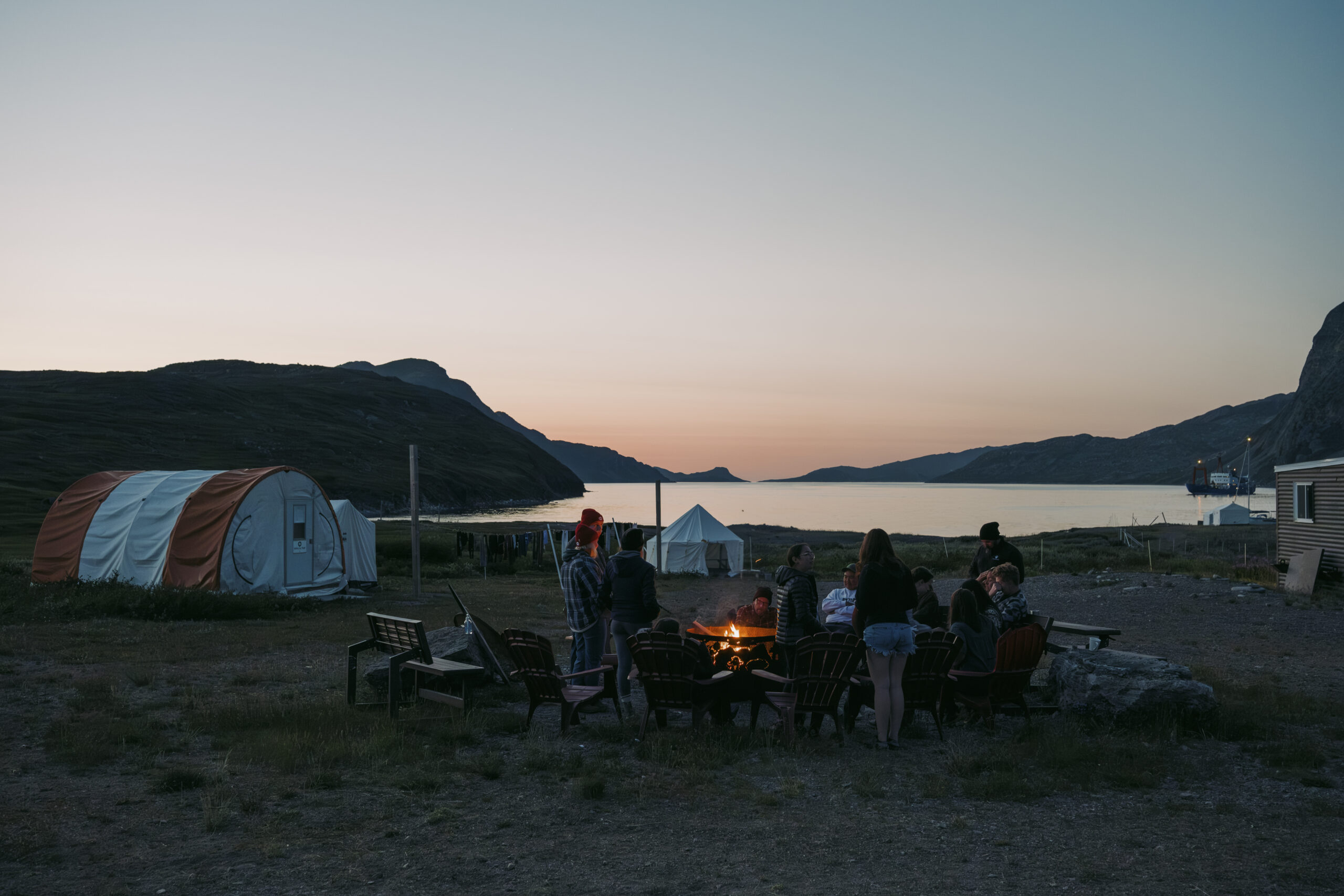 Torngat Mountains National Park: People gather at a campfire as the sun sets on St. John's Bay at Torngat Mountains Base Camp