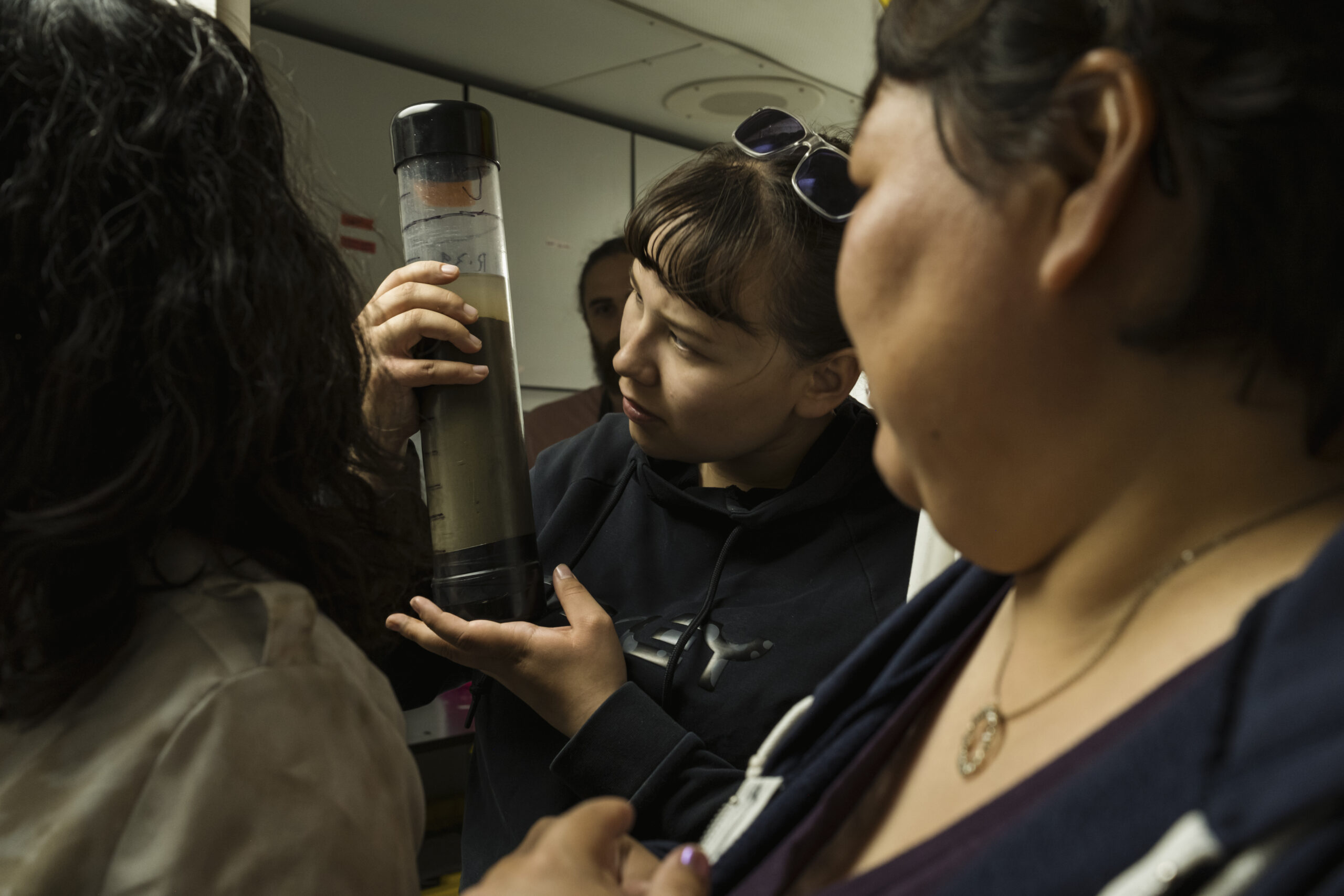Two women look at a plastic tube full of mud.
