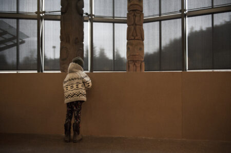 Photo of a boy facing away from the camera, looking at totem poles with Nisga'a artwork on it.
