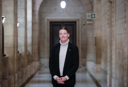 Environment and climate change minister Tracy Schmidt stands in a black blazer and beige turtleneck in a hallway of the Manitoba legislative building