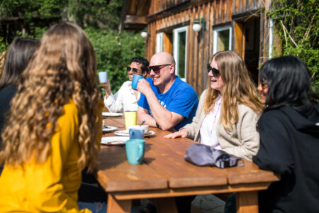 Narwhal journalists sitting at a table outside in the sun, chatting, drinking coffee and laughing.