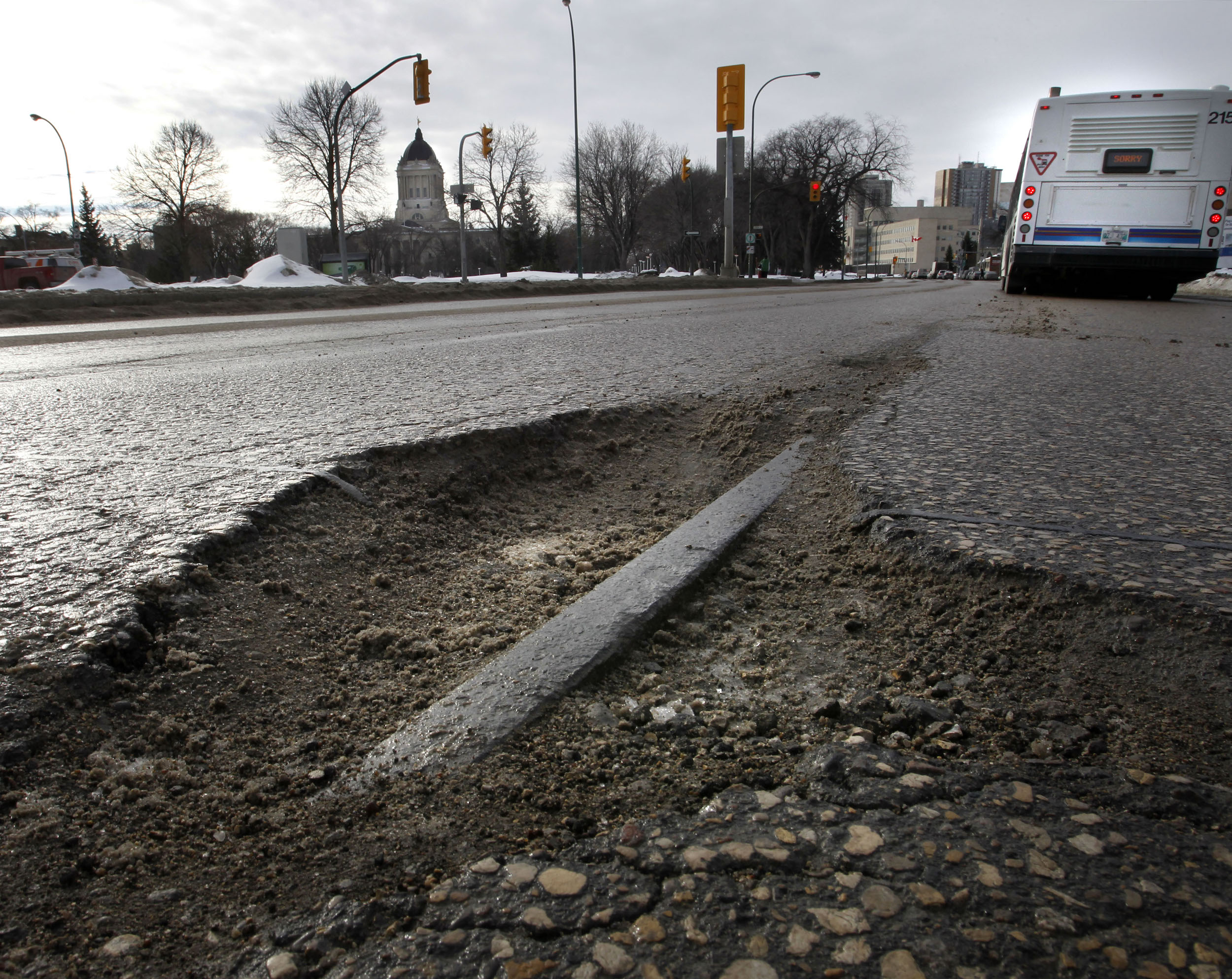 A streetcar rail peeks through a pothole behind a Winnipeg transit bus on Osborne Street near Manitoba's legislature