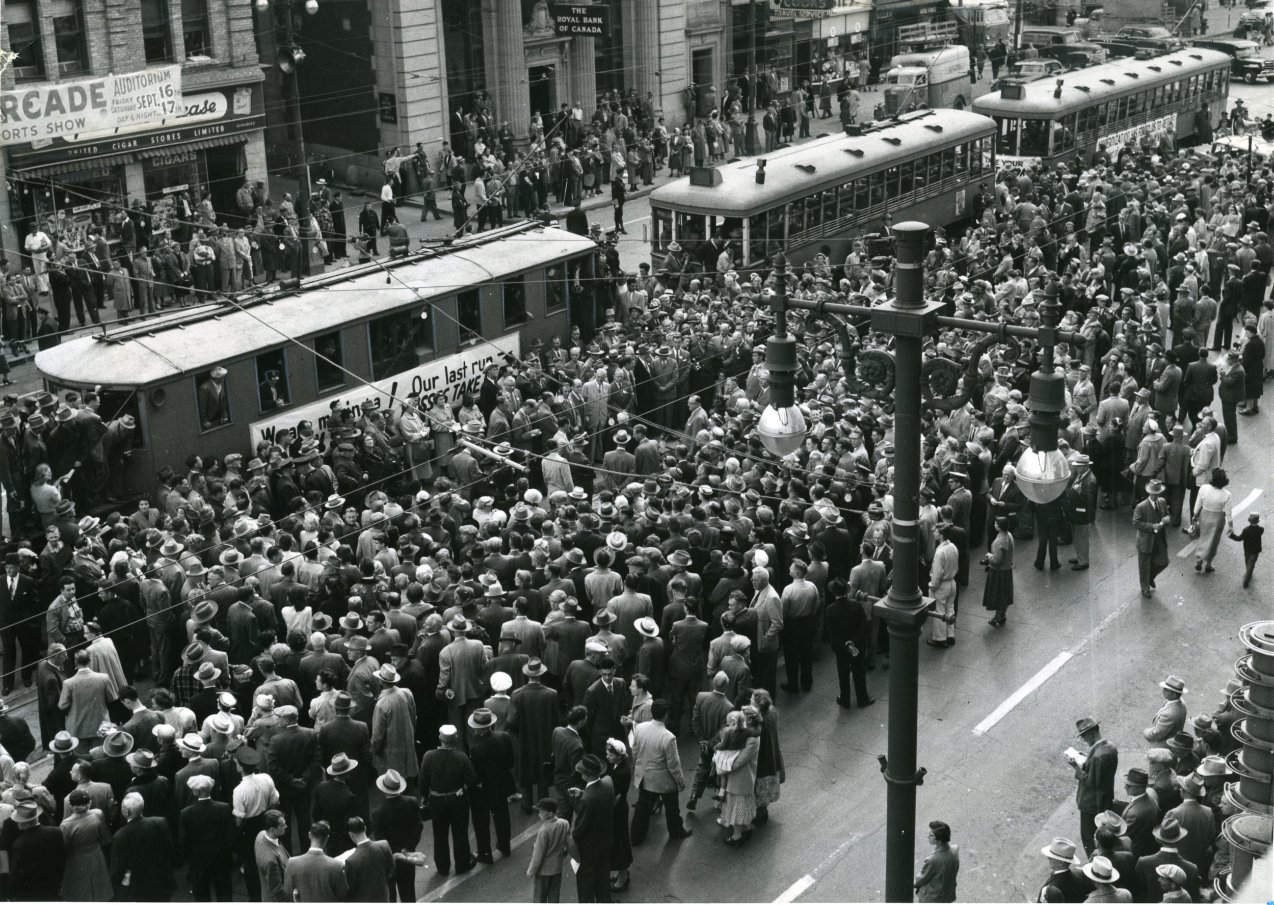 Hundreds of people crowd around a row of streetcars on Portage Avenue in downtown Winnipeg for a ceremony marking the end of the streetcar system in 1955