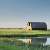 Sun shines on a barn in a farmers field with a pond in the foreground