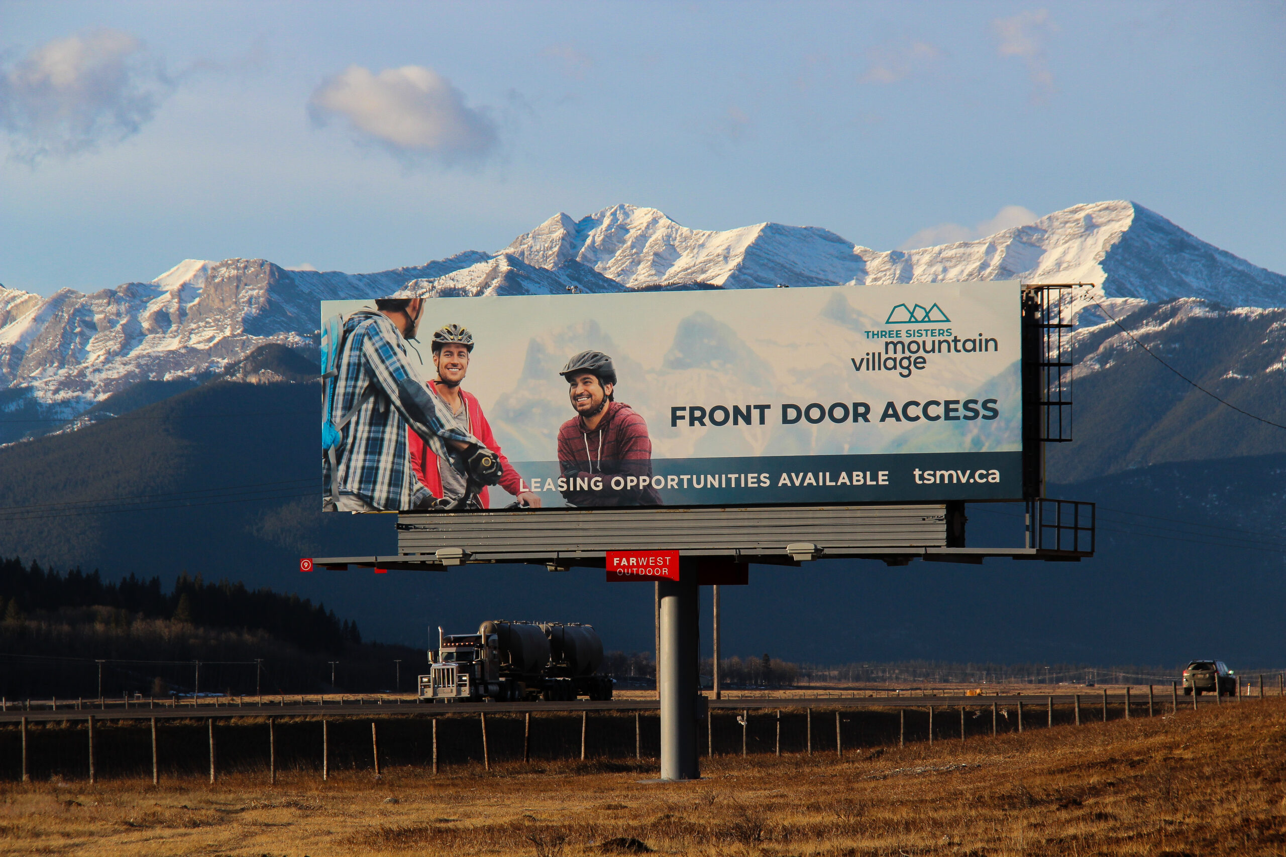 A billboard advertising Three Sisters Mountain Village on the road to Canmore with mountains in the background