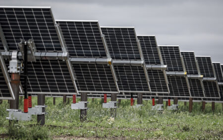 Close view of the backside of solar panels in a field pointing at a grey sky