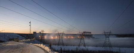 Manitoba Hydro's Limestone dam and generating station glows orange in the background with transmission towers and lines in the foreground