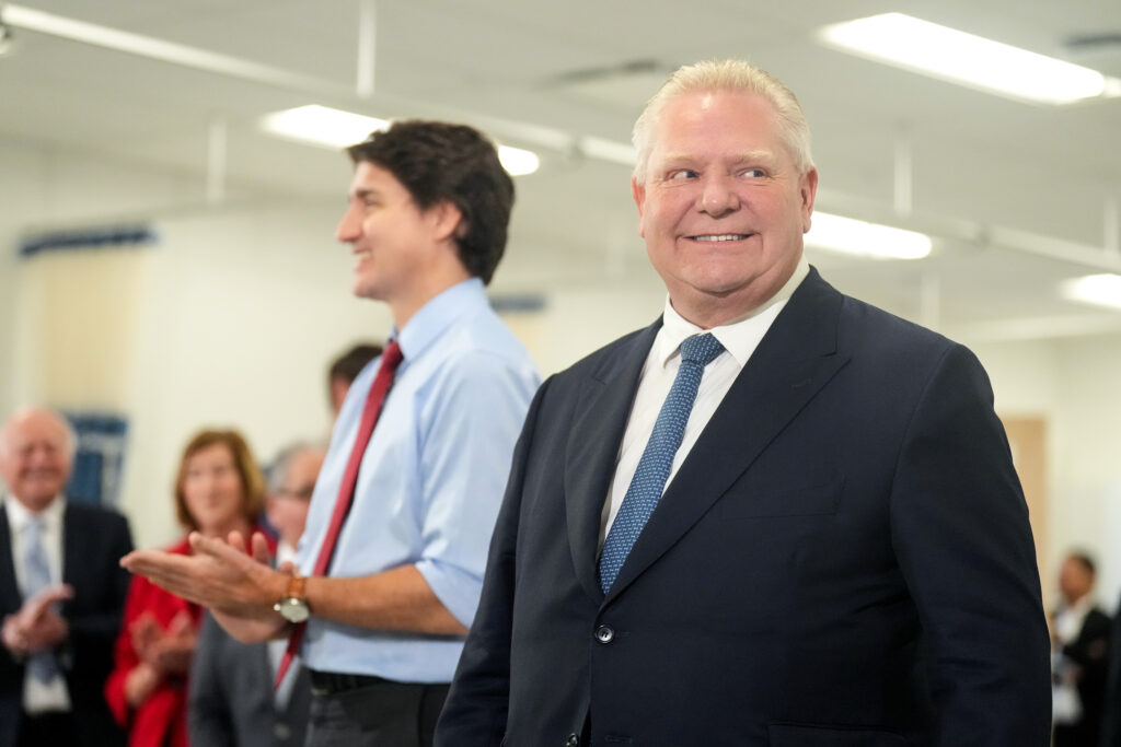 Ontario Premier Doug Ford smiling with Canadian Prime Minister Justin Trudeau behind him clapping