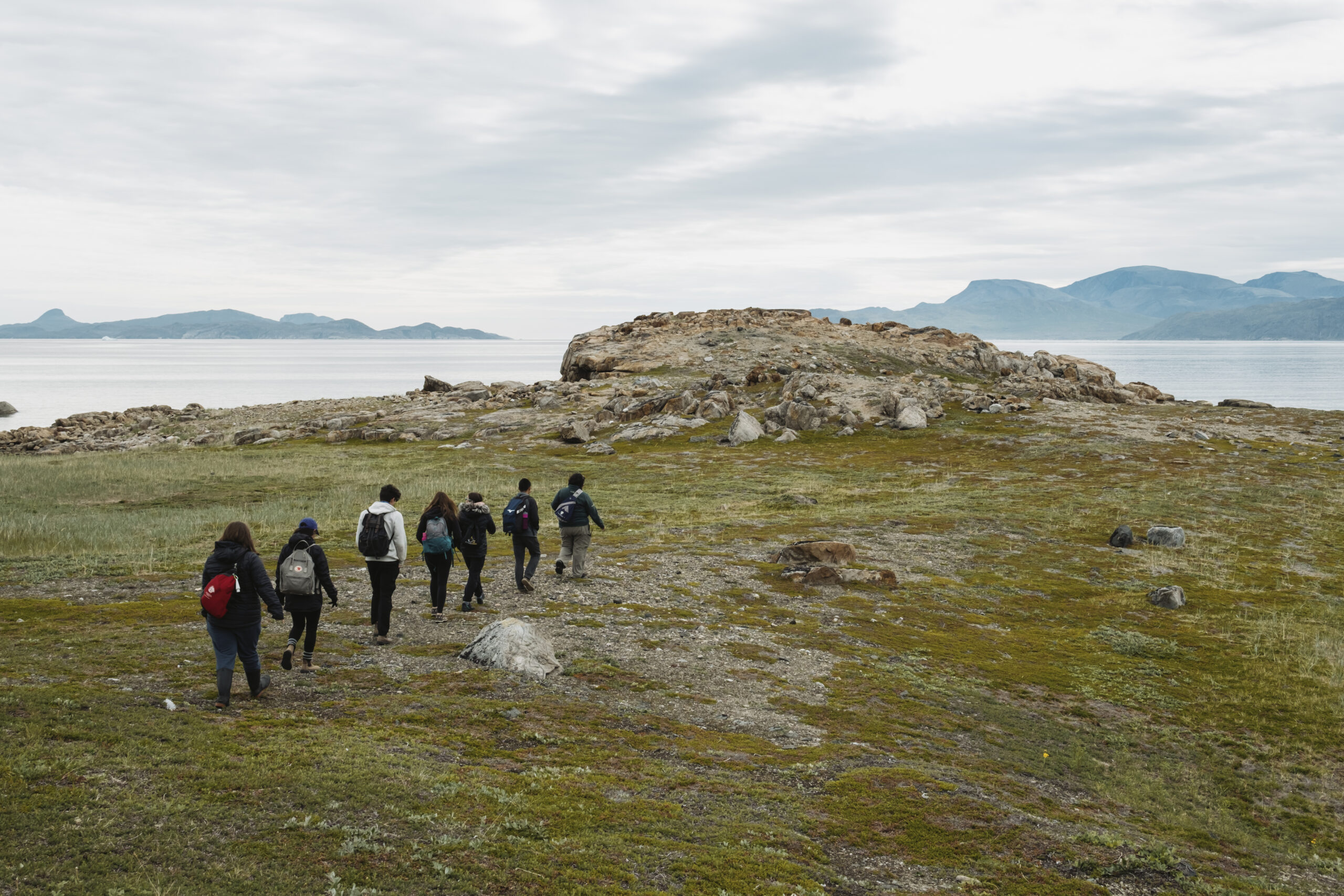 People walk in a line towards a cliff in Torngat Mountains National Park with the Labrador Sea and mountains in the distance