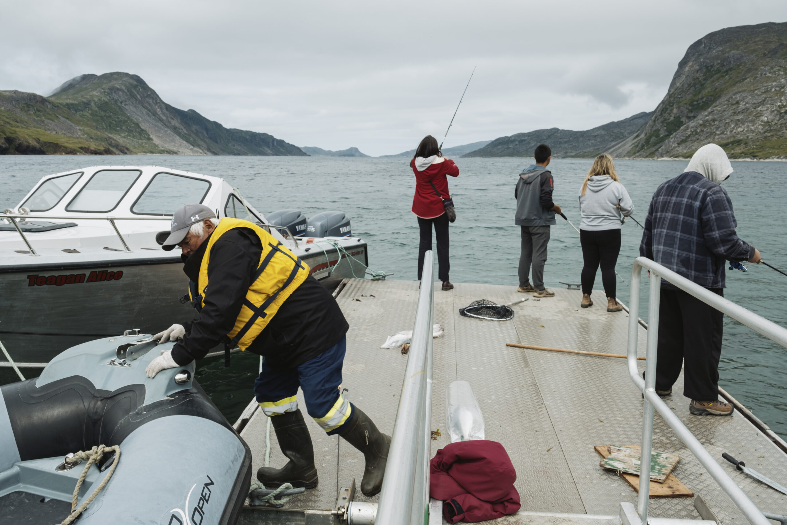 Four people fish from the dock of the Torngats Base Camp in Saglek Fiord while another man pushes a zodiac away from the doc