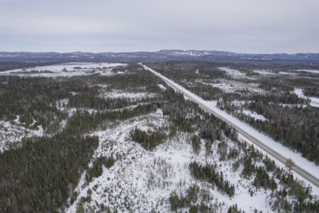 Aerial view of Ontario's Highway 17 cutting through forested terrain with hills in distance