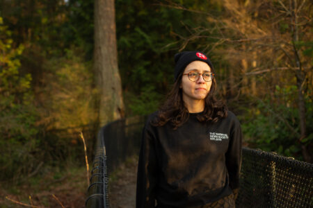 Director of operations and finance Atenas Contreras, in a forest, gazes out wearing glasses and a Narwhal toque and a sweater.