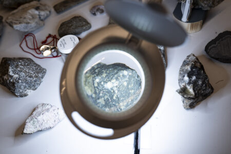 A microscope lens is focused on a rock sample, with various other samples displayed on a white table around it