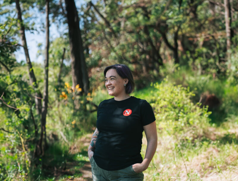 Shannon Waters, The Narwhal's B.C. politics and environment reporter, looks out at the trees wearing a Narwhal shirt.